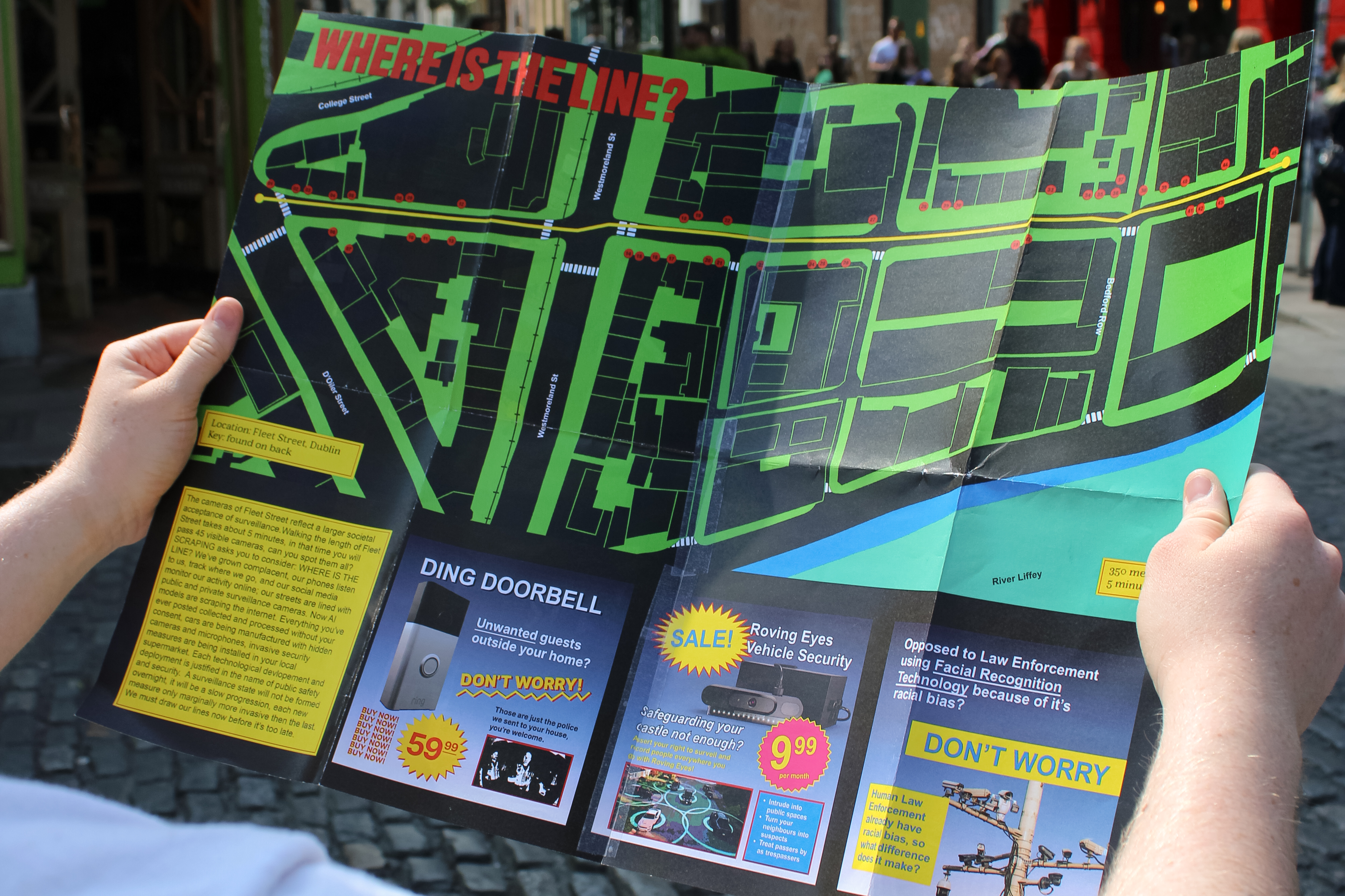 man holds black and green stylised map of Fleet Street all CCTV cameras marked on the map, three kitchy satircal ads about current and emerging surveillance tech are on the bottom of the map