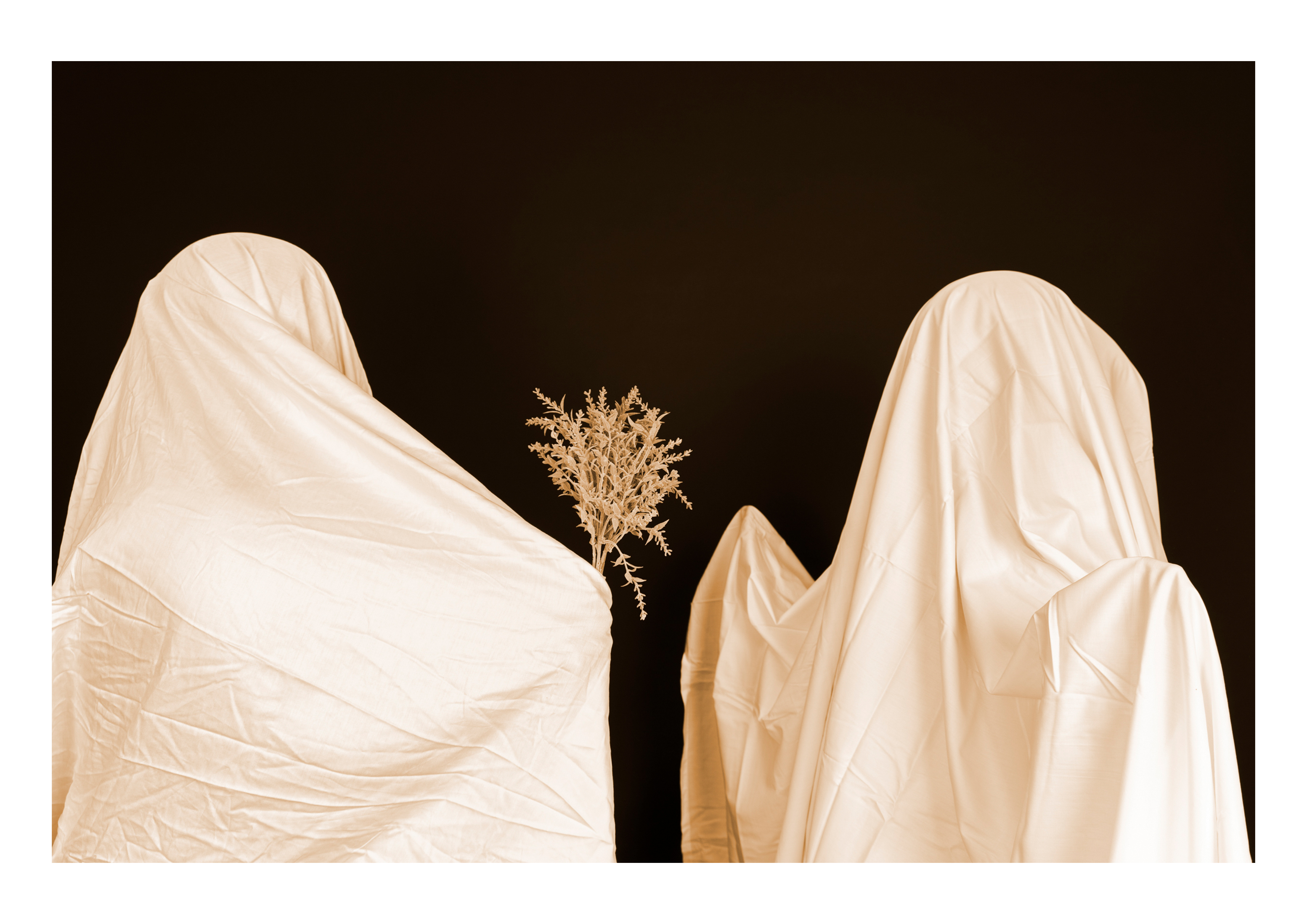 Two people in white sheets, one holding out a bunch of flowers