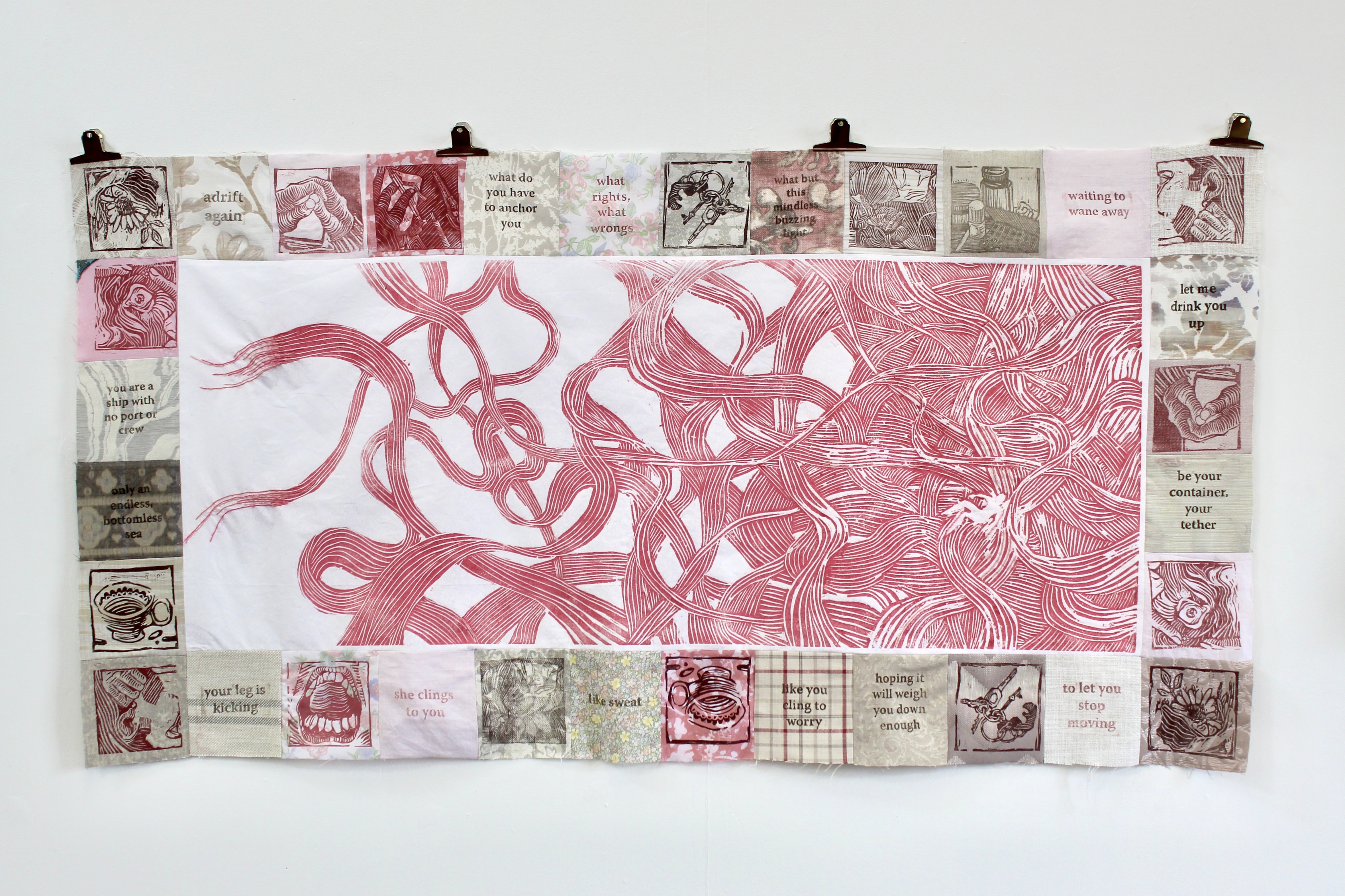 A rectangular tapestry piece. In the centre, there is a long print of pink overlapping lines surrounding a small negative space figure. Around that, there is a border of small squares of fabric stitched together. Each has a print or a small section of text on it.