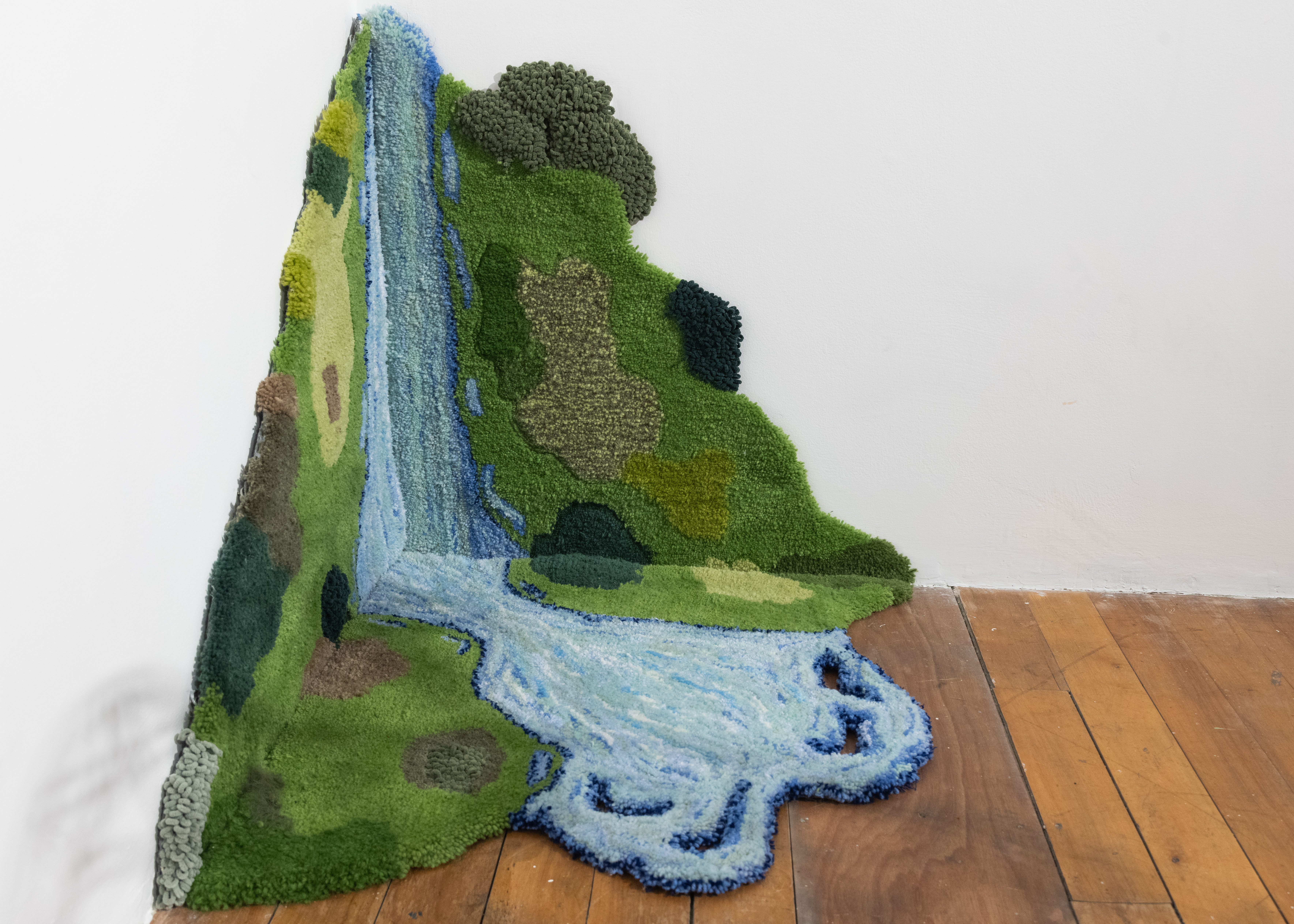 three tufted rugs in a corner depicting a waterfall and greenery.