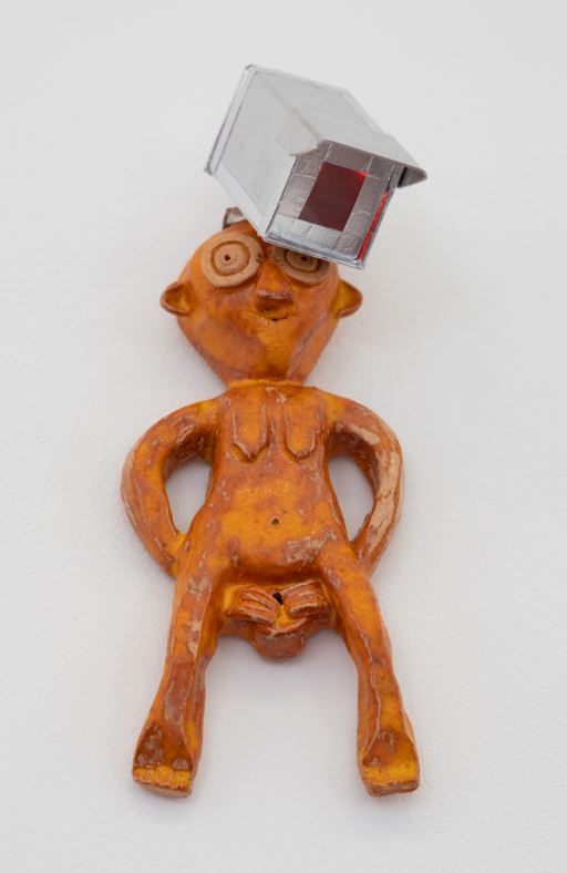 Image of an orange colored Sheela-na-gig with a small CCTV camera on her head