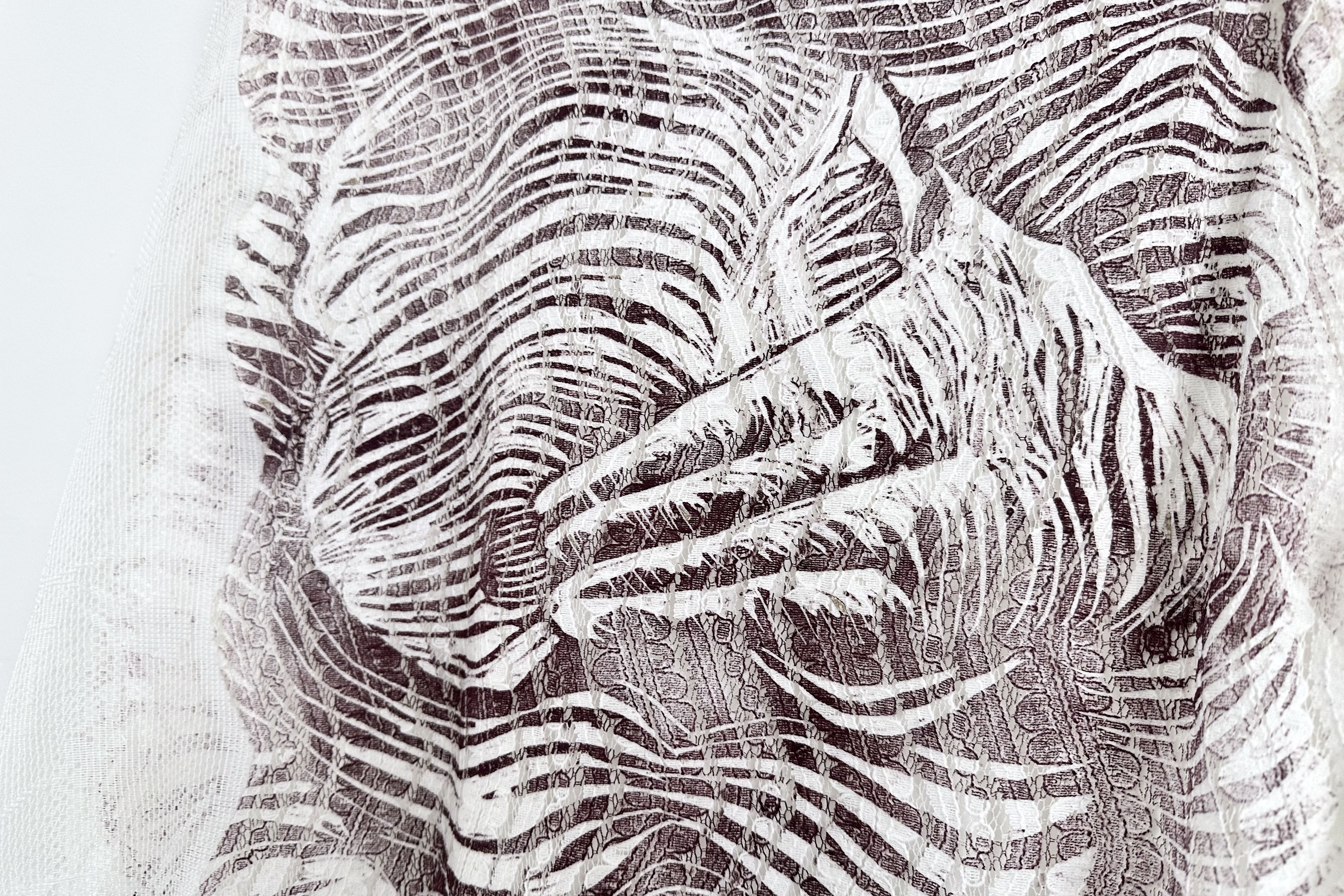 A closeup of a print on a lace dress. A hand is depicted covering a woman's torso, with the lace underneath texturing the print.
