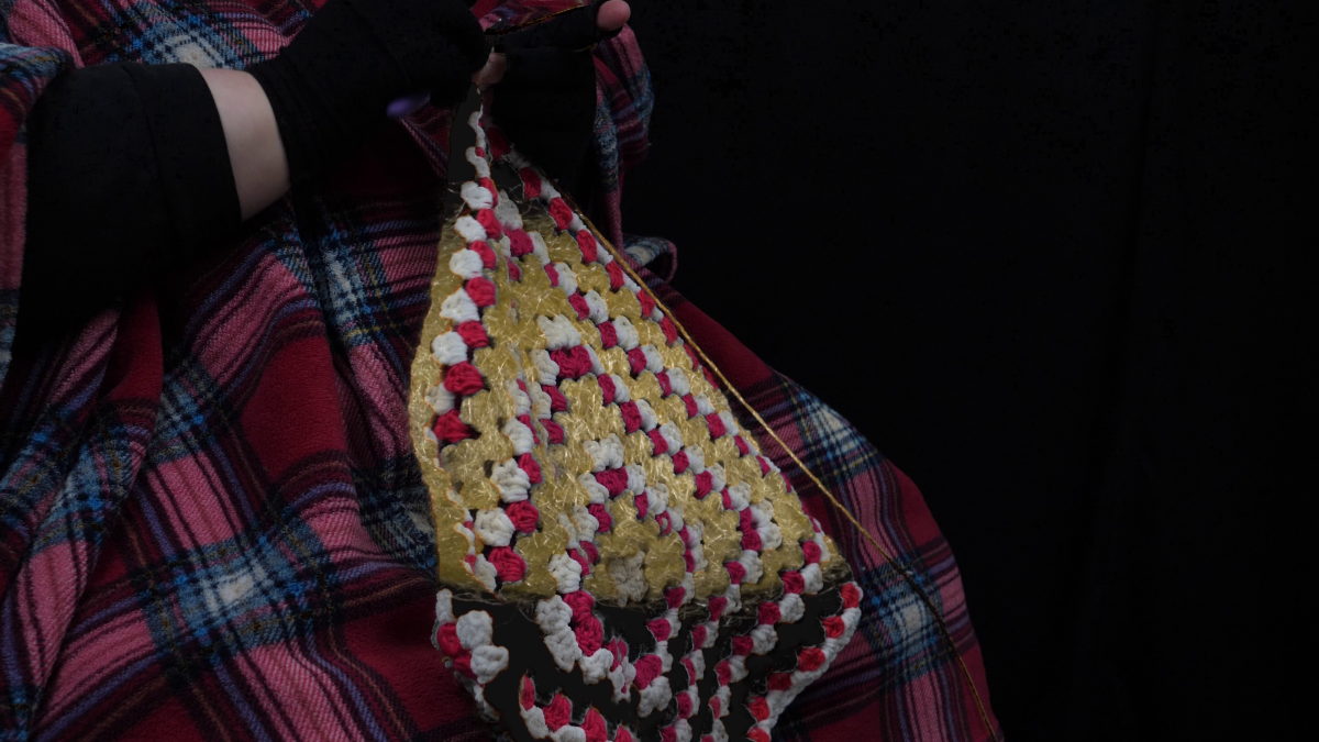 Still of Logan Valentine hands and torso crocheting the cocoon in cripteron with an actual cocoon keyed into the crochet project