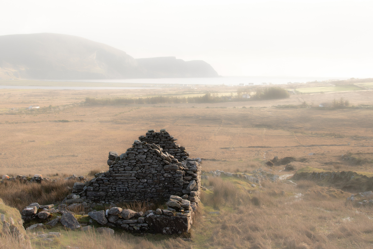 A stone cottage with only the gable wall standing in a vast landscape with a mountain in the background