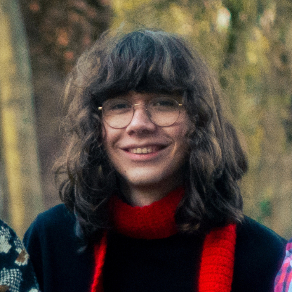 Photo of Erik with long brown hair and round glasses, wearing a red scarf, smiling.