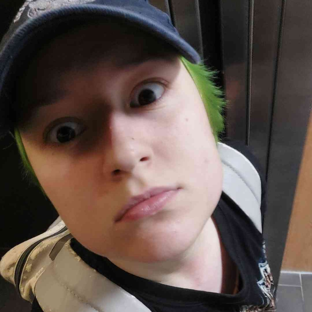 a guy with green hair and an air force cap staring at the camera from a high angle with wide eyes and a straight face