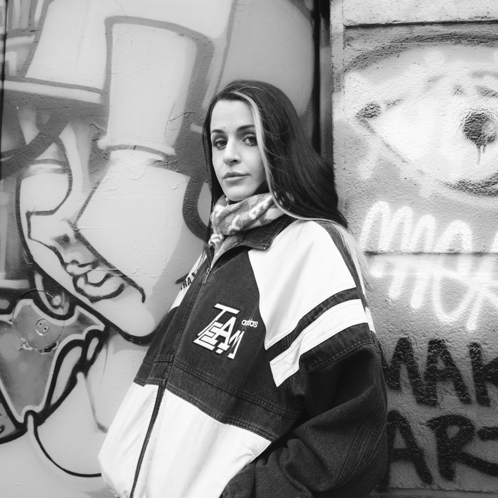 This black and white photograph pictures the artist leaning against a graffiti wall and turning towards the camera